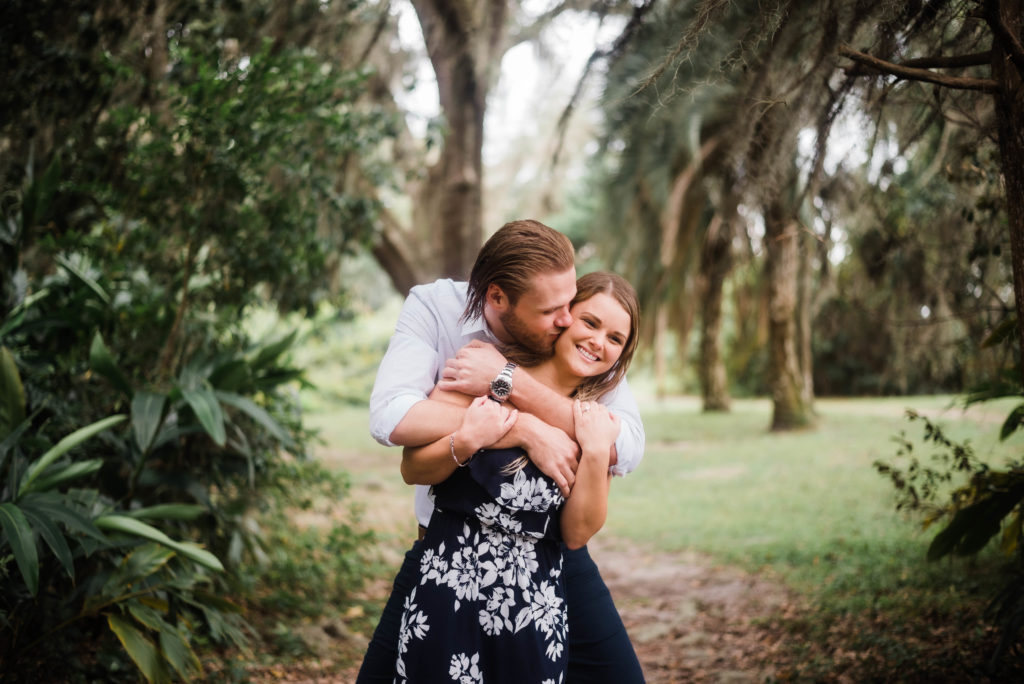 Groom hugging his bride during engagement photo in front of the Bennett House,  Alpine Groves Park. in Jacksonville Florida  Photo By Black Tie & Co. www.btcweddings.com