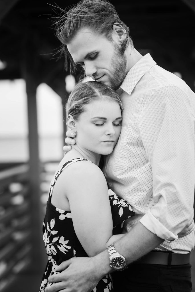 Groom hugs bride while taking engagement photo the dock of the St Johns River at the   Alpine Groves Park. in Jacksonville Florida  Photo By Black Tie & Co. www.btcweddings.com