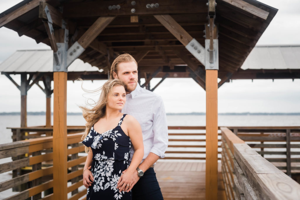 couple looking out at the river taking engagement photo the dock of the St Johns River at the   Alpine Groves Park. in Jacksonville Florida  Photo By Black Tie & Co. www.btcweddings.com