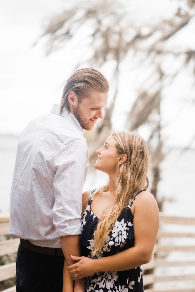 couple looking at each other while they are taking engagement photo the dock of the St Johns River at the   Alpine Groves Park. in Jacksonville Florida  Photo By Black Tie & Co. www.btcweddings.com